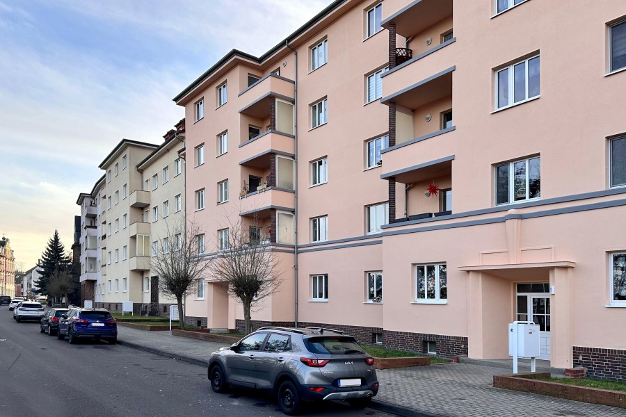 Mehrere mehrstöckige Wohnhäuser in einem Wohngebiet mit einer Straße und parkenden Autos davor.