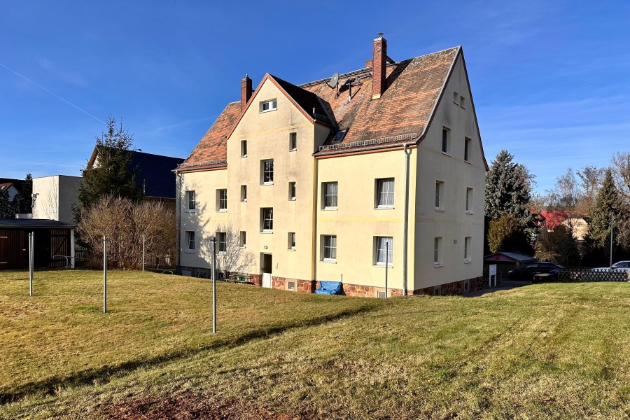Kleines mehrstöckiges Mehrfamilienhaus mit Wiese und Wäscheplatz davor bei blauem Himmel und Sonnenschein.