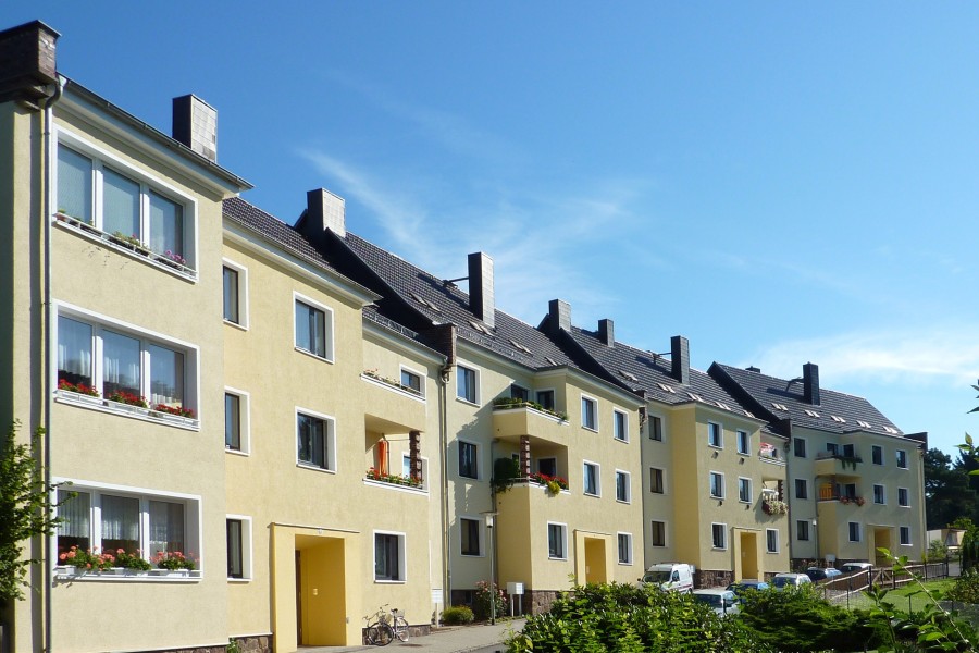 Großenes, mehrstöckiges Mehrfamilienhaus vor einer Straße mit Hecken