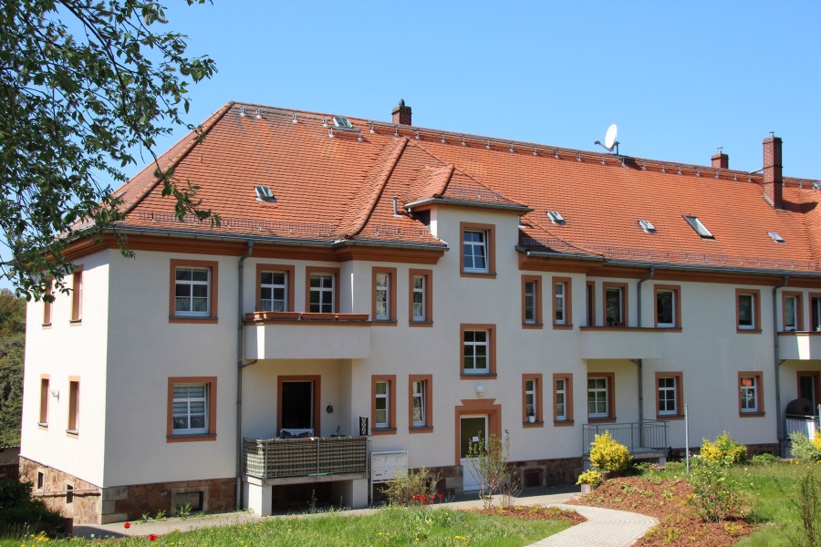 Zweistöckiges Mehrfamilienhaus mit teilweise Balkonen, davor Wiese und gepflegte Beete.
