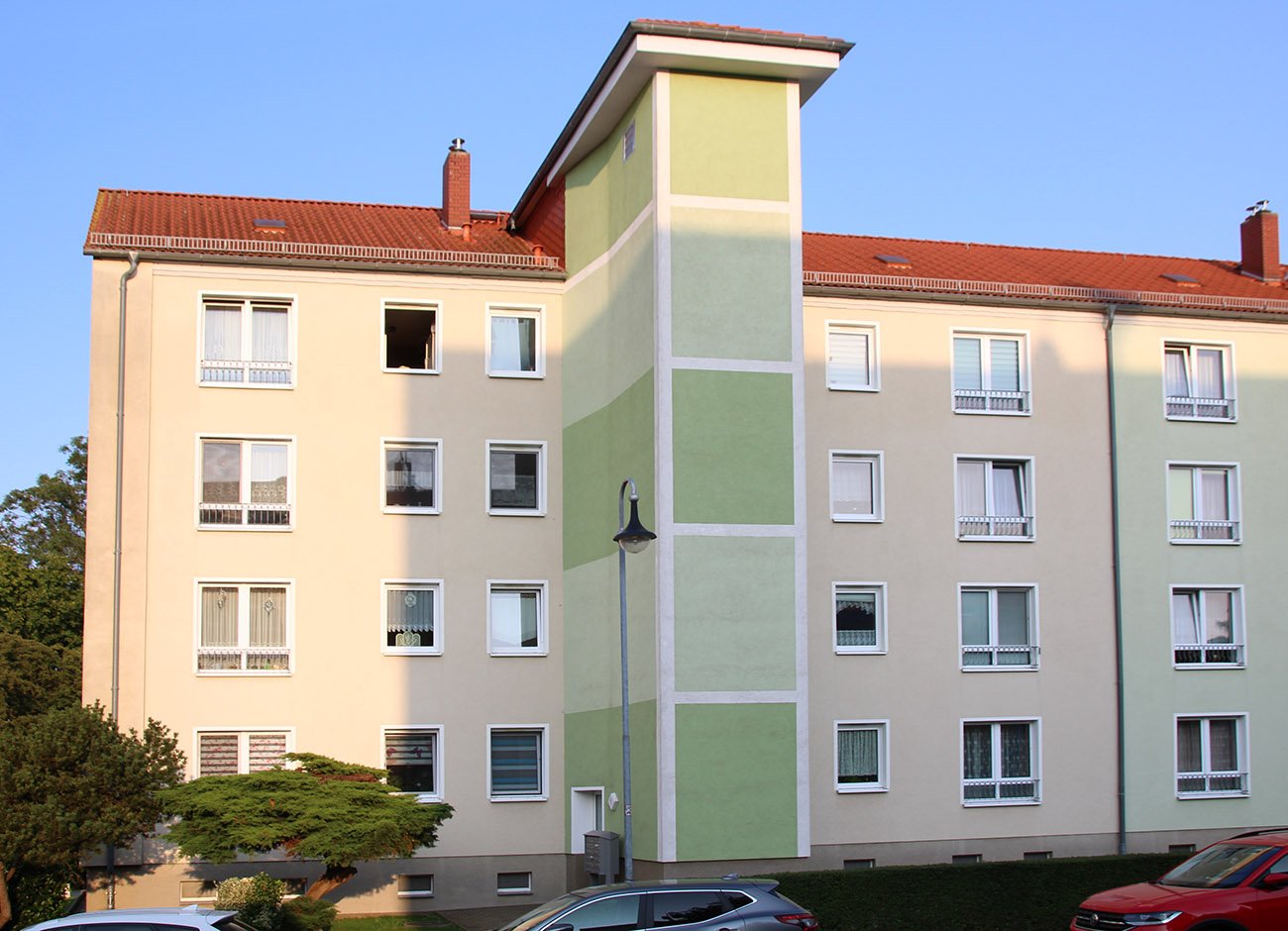 Vierstöckiges Mehrfamilienhaus, blauer Himmel und davor kleine Bäume.